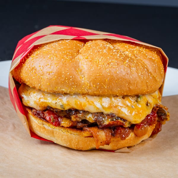 Gardner's Grill cheeseburger with melted cheese, bacon, and red sauce, wrapped in red and brown paper.
