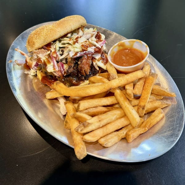 Pulled pork sandwich with coleslaw and barbecue sauce, served with a side of french fries.
