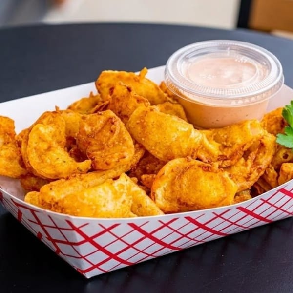Crispy fried potato wedges in a red and white checkered paper tray with a side of dipping sauce.