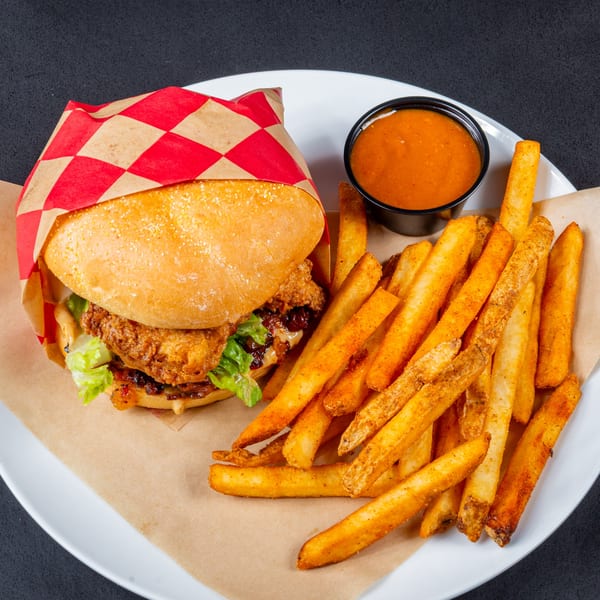 Gardner's Grill fried chicken sandwich with lettuce, sauce, and a side of seasoned fries and dipping sauce.