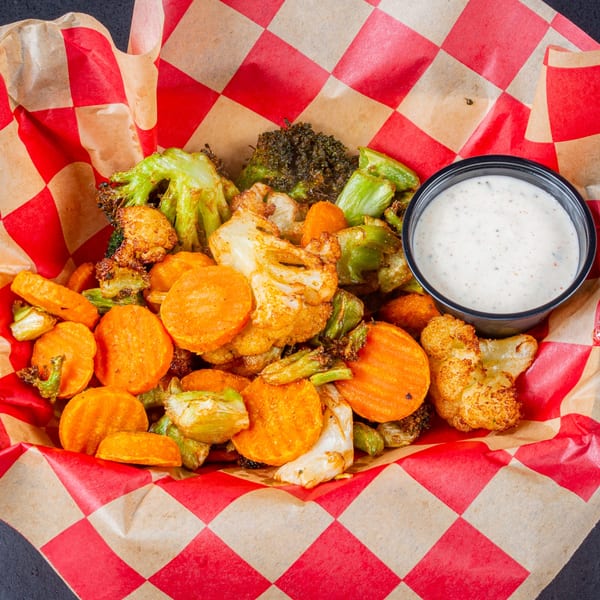 Roasted carrots, broccoli, and cauliflower with a side of ranch dressing in a checkered paper-lined basket.